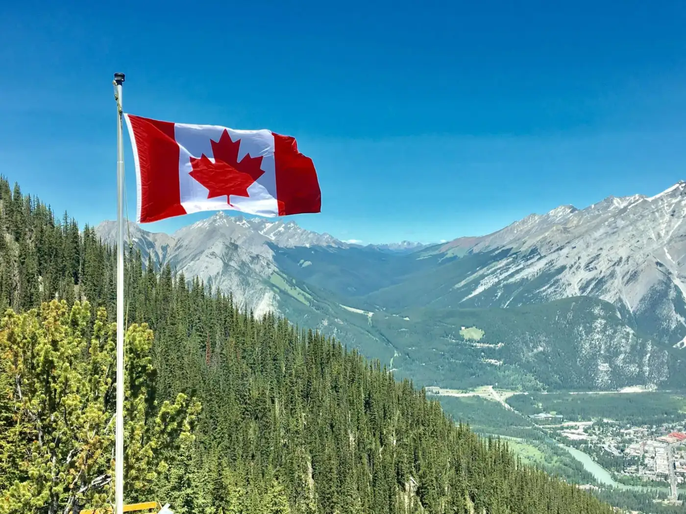 Flag of canada on pole, grass, and mountain
